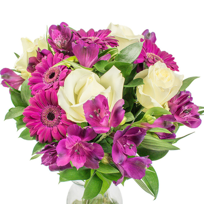 A lush, professionally tied round bouquet displayed on a clean white field, where creamy white roses and a trio of deep magenta Gerbera daisies create a striking, elegant contrast. The roses are soft and tightly furled at their centres, the layered petals opening outward in a classic, romantic spiral that suggests a quiet fragrance. Dominating the colour story are at least three Gerberas in a vivid magenta-pink, their broad, satiny petals mapping out a cheerful geometry around dark, almost black centres that anchor the eye. Interspersed between these larger blooms are abundant clusters of purple and fuchsia Alstroemeria-Peruvian lilies-whose slender, trumpet-like petals often carry subtle speckles and vein-like streaks that introduce fine detail and depth. The bouquet is generously backed with dark green foliage, including broad glossed leaves and some variegated textures that catch light and produce an interplay of highlights and shadow across the arrangement's rounded silhouette. A slim hint of a clear glass vase is visible at the very bottom, grounding the composition and allowing stems to add a vertical rhythm beneath the rounded mass of flowers. Shot in bright, neutral lighting that makes the colours pop against the white background, the arrangement reads as fresh, full, and thoughtfully composed. This centerpiece suits celebratory tables, thoughtful gifts, or an elegant addition to a reception area near City Road or the Barbican, offering an accessible, metropolitan elegance crafted with the steady hand of a local artisan.