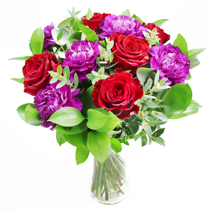 The photograph showcases a beautifully balanced bouquet that brings together classic romance and contemporary styling, echoing the character of Finsbury's mix of tradition and modern city life. At the centre, deep red roses command attention, their petals smooth and velvety, unfolding in graceful spirals that draw the eye into the heart of each bloom. Their rich, almost wine-like hue conveys a sense of sincerity and depth of feeling. Woven among them are lush purple peonies, each flower full and round, with layers upon layers of softly ruffled petals that catch the light at different angles, creating gentle highlights and shadows that give the arrangement a painterly texture. The flowers are cradled by an abundant foundation of greenery. Glossy green leaves curve outward from the base and sides, adding both volume and a feeling of freshness, as though the bouquet has just been gathered from a garden. Slender stems of eucalyptus arch through the arrangement, their soft, silvery-green leaves introducing a cool, modern note that keeps the palette crisp and sophisticated. All of this is anchored in a simple, clear glass vase that reveals the natural lines of the stems, neatly cut and set at varying angles, submerged in clear water. The light in the image is gentle, as if coming from a nearby window overlooking Finsbury's side streets, allowing the reds to glow and the purples to deepen without harsh glare. You can almost sense the scent: a tender, romantic rose fragrance mingling quietly with the refreshing green aroma of foliage and eucalyptus. This is the sort of bouquet that would feel at home gracing a table during an anniversary meal, a special birthday, or an intimate celebration in a Finsbury home, adding both drama and graceful calm to the space.