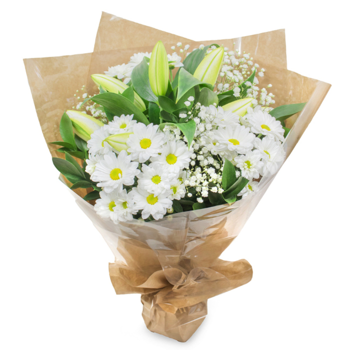Set against a completely white background, this hand-tied bouquet appears almost to float, its fresh whites and greens brought into sharp relief, as though just finished on a workbench in a Finsbury backstreet studio. A broad cluster of white daisy-like chrysanthemums forms the heart of the arrangement, each bloom made up of smooth, narrow petals that curve slightly towards a vivid yellow-green centre, giving a soft, glowing focal point. These blooms are massed together so that their edges gently touch, creating a rounded, cushion-like effect that feels both generous and soothing. From within this calm surface, several long, slender lily buds emerge, still tightly closed. Their surfaces are sleek and smooth, shaded in subtle tones of pale green melting into cream along the tips, and they point upward in a way that suggests hope, promise, and patience. Fine sprays of white baby's breath dance through the arrangement, their tiny flowers like scattered snowflakes that soften and lighten the overall design. Encircling the central flowers, an array of deep green leaves, glossy and firm, provides a strong visual frame and enhances the purity of the whites. The bouquet is cradled in a wrap of brown kraft paper, gently crumpled and folded into a cone shape, which brings a rustic, natural charm that feels at home on a Finsbury kitchen table or sideboard. Over this sits a snug layer of clear cellophane, which catches a few highlights and shields the delicate petals while still revealing the textures beneath. At the base, the materials are pulled tight around the stems, forming a neat handle. The overall mood is tranquil and reverent, an ideal expression of sympathy or quiet support for families and friends throughout Finsbury and the surrounding streets.