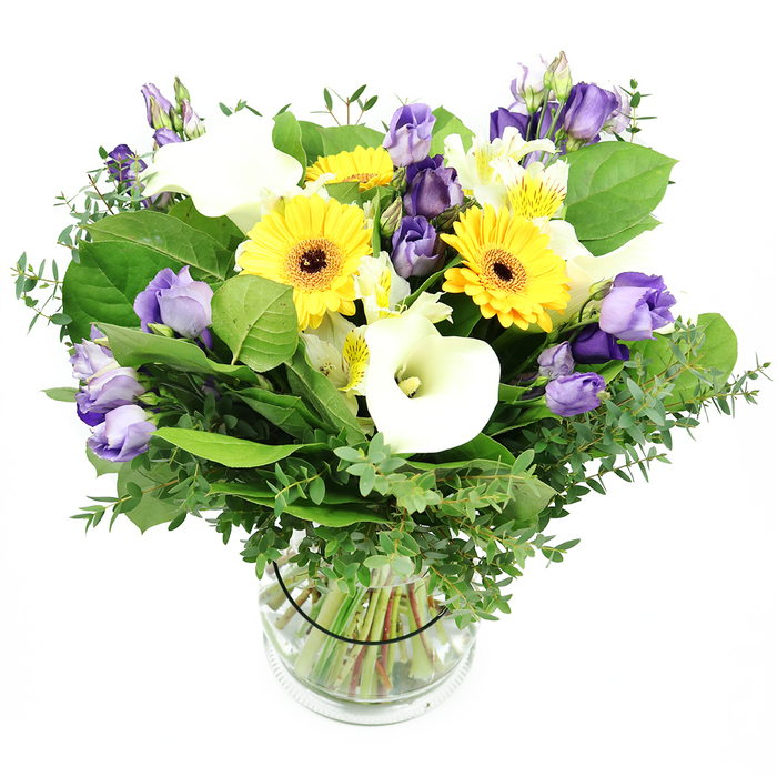 An elegant hand-tied mix of yellow, white, and purple blooms gathered in a clear glass vase sits against a bright white backdrop. The bouquet centers on large yellow Gerberas with dark centers, radiating sunshine across the arrangement. Pristine white Calla lilies rise in proud, sculptural trumpet shapes, lending a contemporary edge. Clusters of soft lavender Lisianthus weave through, some fully open and others in bud, giving depth and gentle curves that invite the eye to wander. White Alstroemeria with subtle yellow markings brighten gaps and catch fleeting light, while a lush green foundation of eucalyptus sprigs and broad leaves adds texture and life. The glass vase reveals neatly trimmed green stems submerged in water, and a slim black band secures the stems inside, preserving the bouquet's clean, architectural line. This premium design reads as a refined celebration-joyful, pure, and perfectly suited for birthdays, anniversaries, or hospitality spaces in a home or office. From Finsbury Flowers, delivery is available across Finsbury, Islington, Clerkenwell, and surrounding neighbourhoods, with options for same-day service to brighten a room or mark a special moment. The bouquet's bright palette and poised structure make it a versatile centerpiece, easily adapting to festive occasions or calm, everyday elegance in a small urban flat near the Angel and Upper Street.