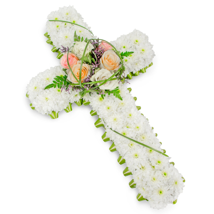 Here, a traditional Christian cross made entirely of fresh flowers is captured against a bright, uncluttered white backdrop, evoking a calm, contemplative atmosphere akin to stepping into a quiet chapel off Pentonville Road. The main body of the cross is formed from numerous small white chrysanthemums, placed shoulder to shoulder so that their tiny petals overlap, creating a dense, cushion-like texture. This expanse of white blooms imparts a powerful sense of purity, innocence, and peace, flowing seamlessly from the top of the cross down to the base. Encircling this field of white is a fine border of lush green foliage that runs unbroken around the edges. This vibrant green edge clearly defines the well-known shape of the cross, adding both structure and a gentle touch of nature's freshness, reminiscent of tree-lined paths and courtyard gardens scattered throughout Finsbury and Clerkenwell. At the centre, where the horizontal and vertical sections meet, a gently raised focal cluster offers a warmer, more personal feeling. Several roses in soft peach, coral, blush pink, and creamy ivory are nestled together, their fully opened petals curving outward in generous spirals. They are interwoven with feathery fern, slim loops of bright green grass, and lightly scattered purple filler flowers, which add a hint of colour depth and a more organic, garden-like texture. The overall composition is harmonious and respectful, the kind of floral cross often chosen for funeral services or memorial gatherings in local churches and crematoria. It visually expresses sympathy, faith, and remembrance for families in Finsbury, Angel, and surrounding North London communities.
