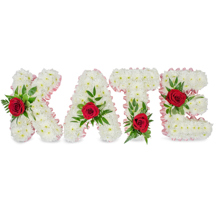 Set against a clean white backdrop, this elegant floral tribute spells the name KATE in bold, three-dimensional block letters, each letter built from an abundant, tightly packed layer of small white chrysanthemums. The chrysanthemums' tiny petals create a soft, cloud-like surface that conveys purity and calm while preserving the distinct geometry of each letter. A slim pale-pink satin ribbon is pleated and applied along the outer edges, providing a quiet, decorative border that warms the arrangement without overwhelming its simplicity. Each letter bears a single, vivid red rose positioned as a focal accent - the K's rose is placed low on the left vertical stroke, the A's rose crowns the tip of its peak, the T's rose sits at the base of the left side of the horizontal crossbar, and the E's rose rests squarely on the middle horizontal arm - with each crimson blossom framed by an assortment of lush green foliage including broad glossy leaves and delicate fern fronds. The foliage adds natural movement and depth, shadowing the chrysanthemum forms and enhancing the three-dimensional look. There is a discreet, comforting fragrance: the warm rose perfume tempered by fresh green notes from the foliage and the clean, slightly herbal scent of chrysanthemum. Intended as a bespoke sympathy or memorial piece, this arrangement conveys classic symbolism - white for purity, red for enduring love, and green for renewal - making it suitable for funerals, celebration-of-life services, or memorial displays in chapels and community halls around Finsbury and nearby St Luke's. The overall effect is measured, dignified, and deeply personal, reflecting practiced floral craftsmanship and sensitivity to a family's need for a meaningful farewell.