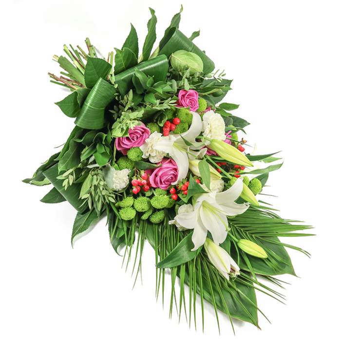 In the heart of Finsbury, this luxurious diagonal floral spray is crafted with the care and artistry emblematic of the area's skilled florists. Set against a pristine white background, it cascades with intentional grace from the top left to the bottom right, mirroring the gentle curves of nearby tree-lined streets. Large white lilies, their trumpet-shaped petals unfurling with golden stamens aglow, form the focal point, surrounded by clusters of vivid pink and magenta roses that bridge the worlds of memory and kindness. Smaller, ruffled white spray carnations are woven in for fullness and texture, softly cradling each larger bloom. Among these, bright green button-like santini chrysanthemums bring a touch of modern vibrancy, offset by the cheery, jewel-like red hypericum berries that nestle among the arrangement's green depths. The foundation of varied greenery-broad, folded leaves, feathered sprigs, and graceful palm fronds falling toward the bouquet's tip-creates a sense of movement and balance, much like the leafy pockets of nearby Clerkenwell. Crafted for tributes, memorials, or moments of solace, this fresh, layered bouquet is offered for same-day delivery across Finsbury, bringing lasting beauty and gentle comfort to every farewell.