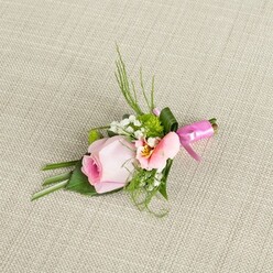 Resting upon a subtly textured, warm beige fabric-evocative of Finsbury's intimate interiors and welcoming cafés-this boutonniere is a harmonious marriage of classic style and local charm. The soft pink central rose, its petals unfurling in a tight spiral, radiates freshness and gentle sentiment, its hue reminiscent of evening blossoms along Amwell Street. Flanking the rose is a creamy peach-toned alstroemeria, its open petals revealing golden accents and faint markings that add depth, not unlike the hidden corners of Exmouth Market. Wispy white sprays of baby's breath lightly scatter throughout, lending an airy elegance, while pops of emerald from miniature cushion mums energise the design. Dark green, blade-like grasses sweep delicately upward, their vividness offset by broader, smooth leaves carefully placed below-one elegantly wrapping the stems for a final flourish. The boutonniere is securely bound with a brilliant, glossy fuchsia ribbon tied into a petite bow, infusing a spirited pink accent that catches the eye. This composition rests on its neutral linen base, every curve and texture emphasized by soft natural light. Ideal for weddings in Finsbury's stately halls, proms, or anniversaries celebrated near King's Cross, this piece captures the artistry, warmth, and freshness that Finsbury Flowers brings to each local occasion.