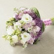 A lush hand-tied bouquet rests on a light-toned, textured table reminiscent of Finsbury's independent cafes, exuding a harmonious marriage of gentle white, lavender, and vibrant green hues. Plush, multi-layered white Lisianthus (Eustoma) command attention at the bouquet's heart, their soft petals radiating peace and elegance synonymous with the tranquil spaces around Amwell Street. Harmoniously blended with them, delicate clusters of lavender and blush-pink stock flowers add dimension and airy movement-each tiny bloom thoughtfully arranged like notes in a classical piece played near Sadler's Wells. Touches of deep purple, starburst Allium inject modern energy and visual intrigue, their spiky forms playful yet refined. Slender, bright green foliage provides volume and freshness, winding through the composition in gentle arcs. The bouquet forms a classic, slightly elongated round, hand-tied by skilled florists and bound with a pastel pink ribbon, subtly striped in white and adorned with tiny white pearls at the knot. Bathed in diffused natural light, every hue and detail stands clear, inviting the imagination to sense fragrant calm and elegant celebration. Whether chosen for a Finsbury wedding, an anniversary toast near Islington, or a momentous gift, this bouquet is shaped by local love and artistry-ready for same-day delivery throughout Finsbury and beyond.